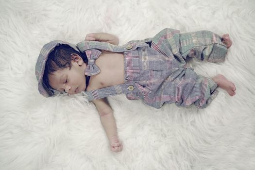 Cute newborn baby in plaid outfit peacefully sleeping on a fluffy white blanket.