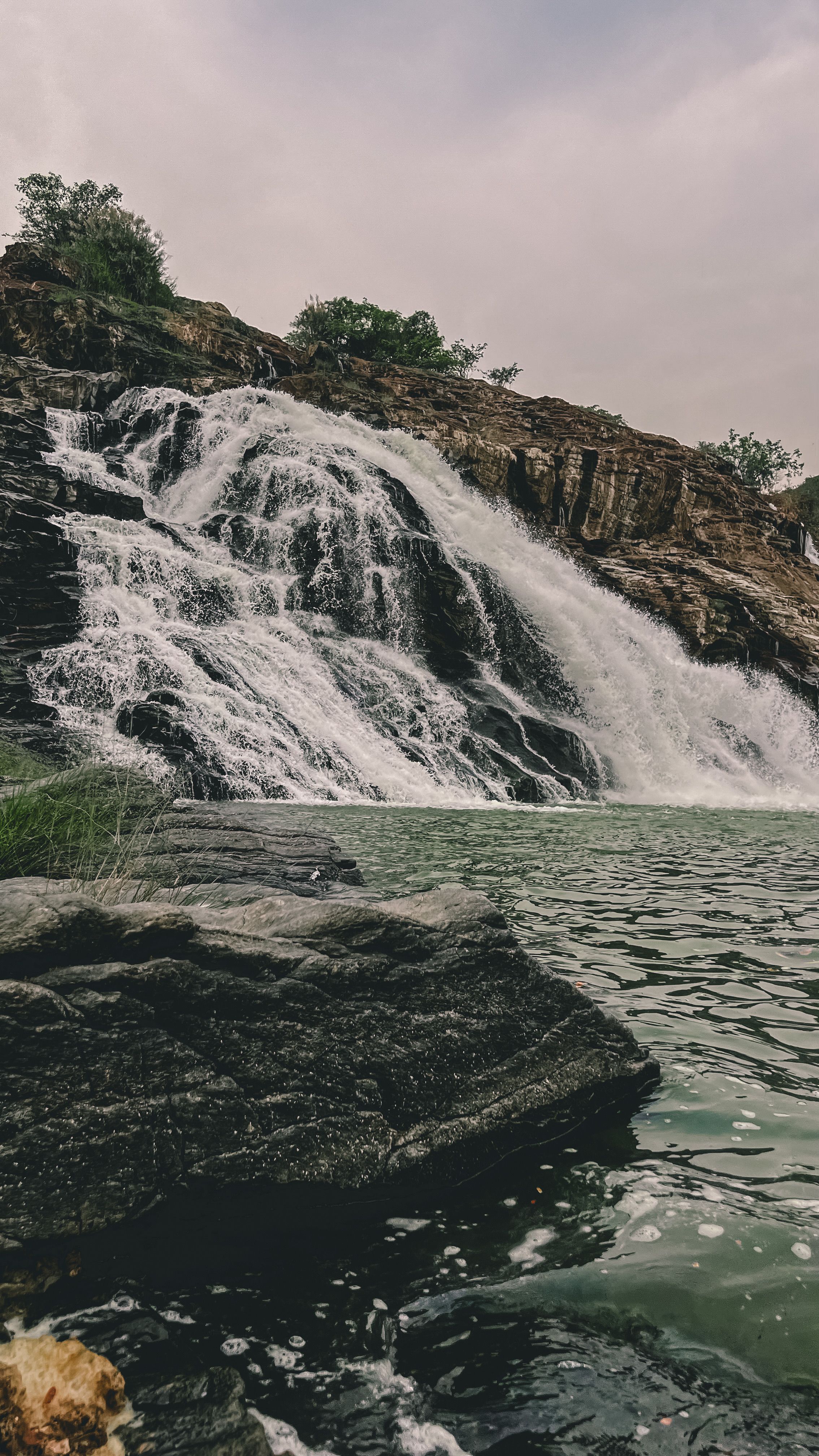 A serene waterfall cascades down rocky cliffs into a tranquil pool, surrounded by nature.