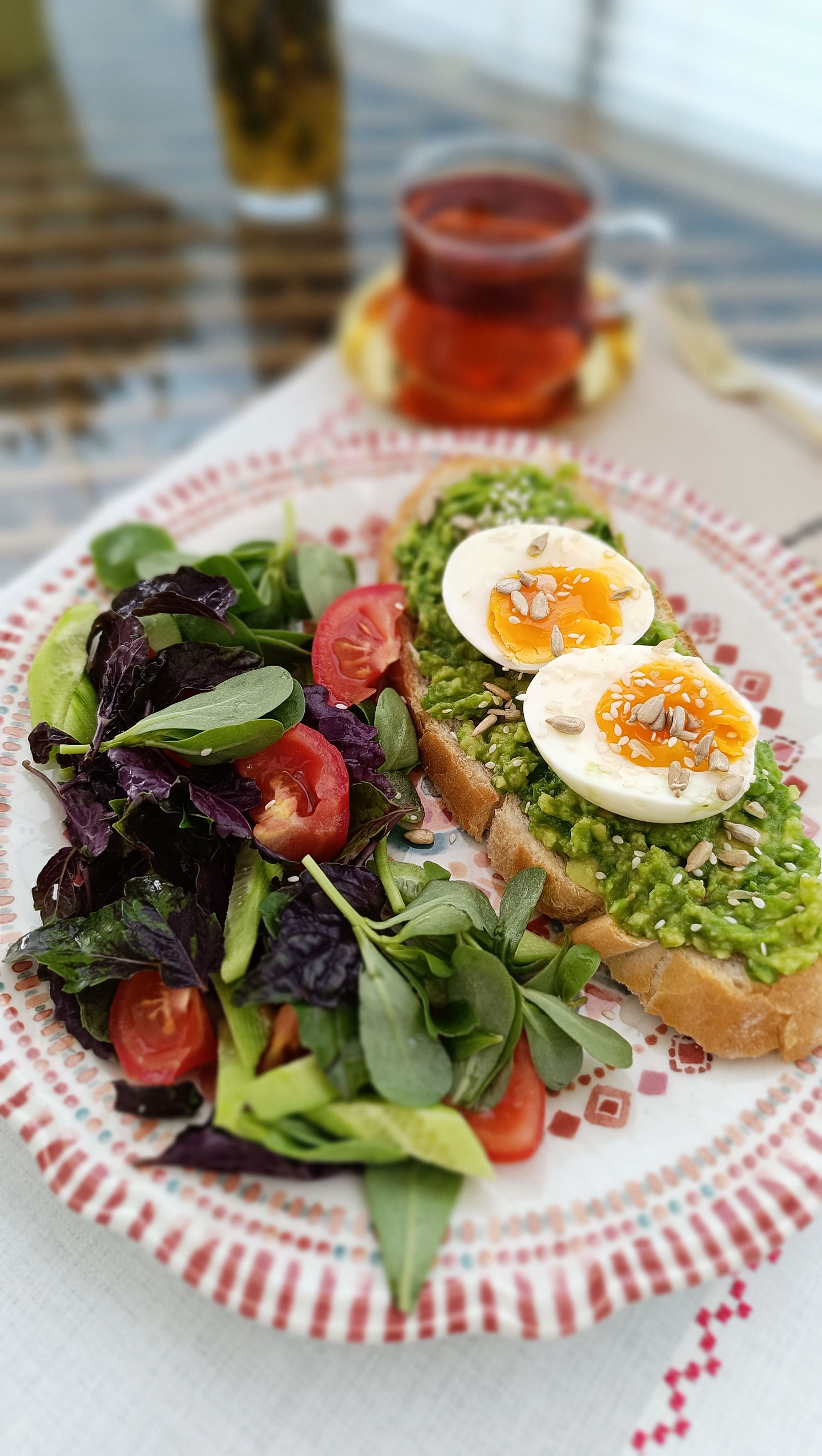 Delicious avocado toast topped with eggs and a fresh salad served with tea.