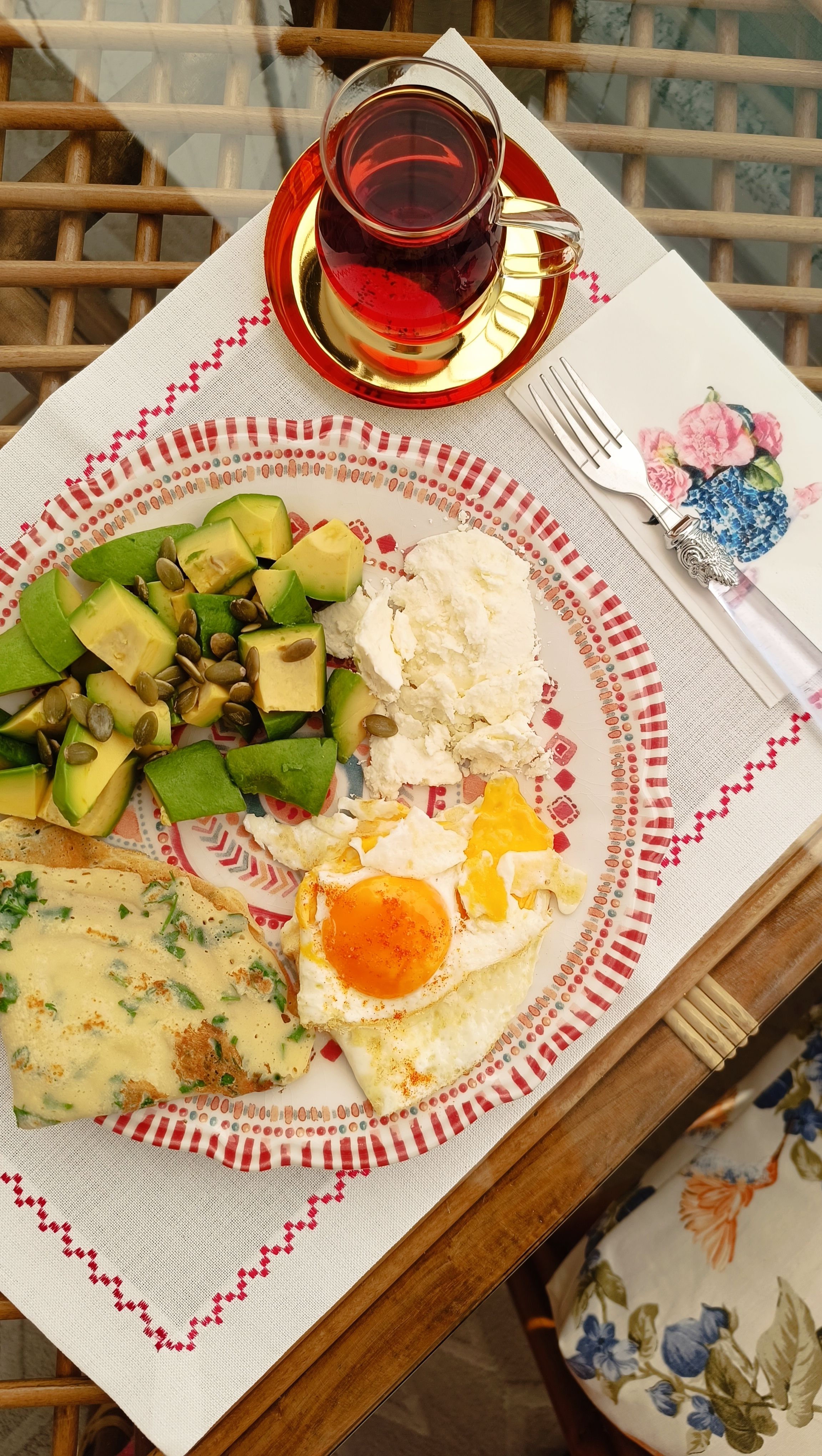 A colorful breakfast plate with eggs, avocado salad, and tea served on a decorated table.