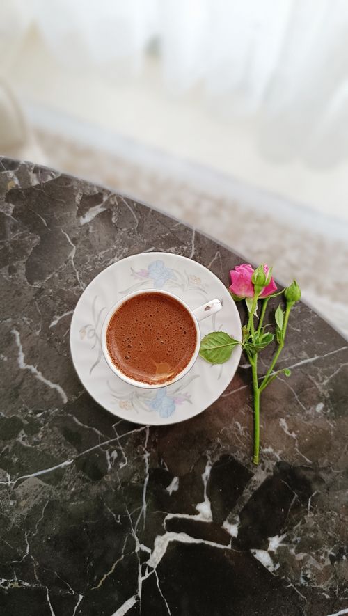 Free Charming scene of a coffee cup with a pink rose on a marble table, exuding elegance and tranquility. Stock Photo