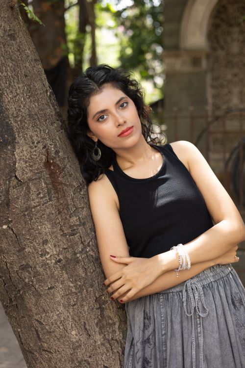Free Stylish young woman leaning against a tree in a sunny outdoor setting. Stock Photo