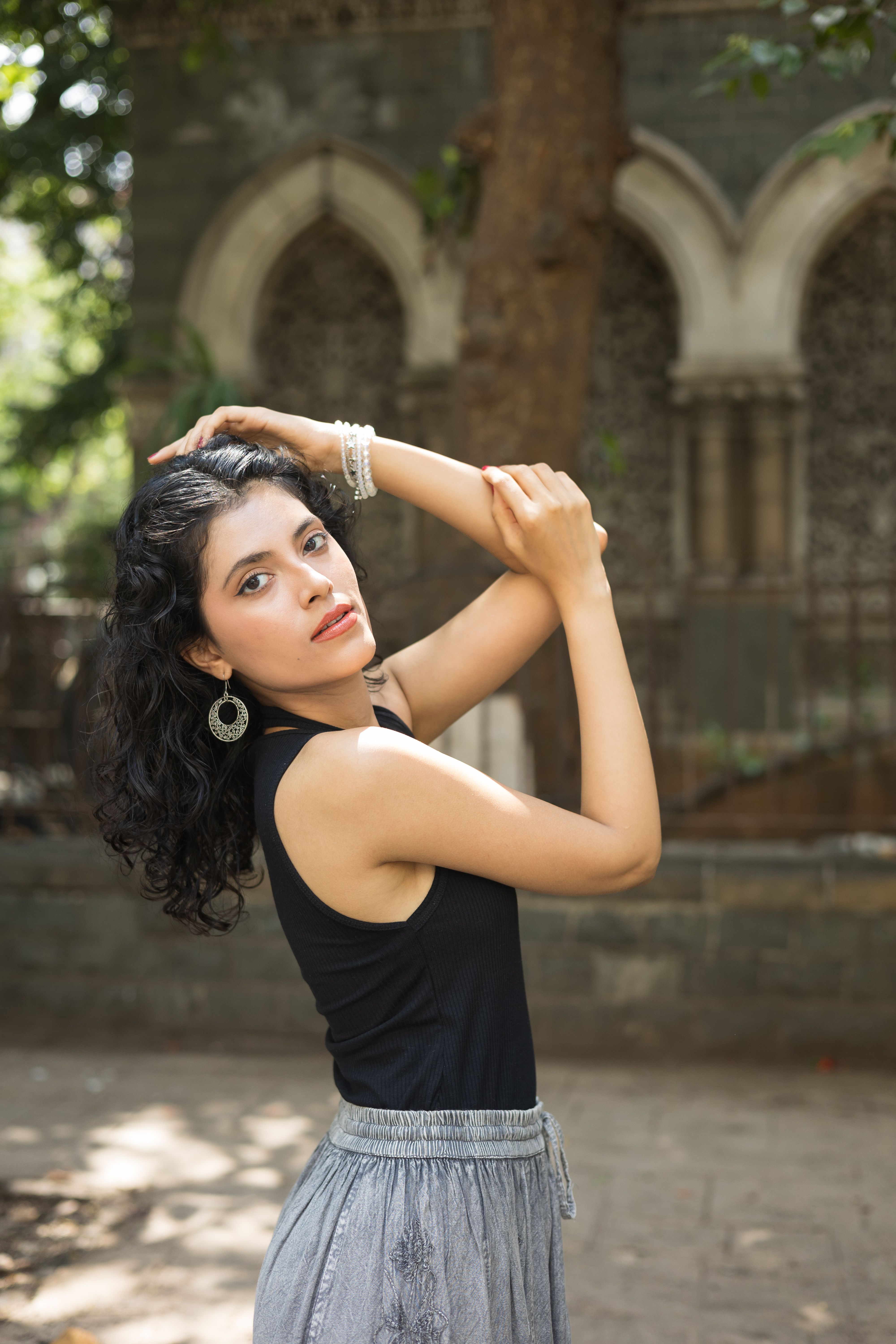 Stylish woman in black top posing gracefully outdoors against an architectural archway.