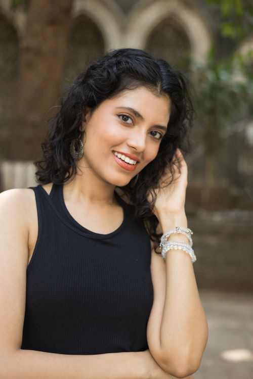 Free Smiling woman posing outdoors, with natural curly hair and stylish jewelry, against blurred background. Stock Photo