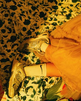 A person in a yellow dress and sneakers relaxing on a floral bedspread in warm light.
