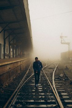 A man walks along foggy railway tracks at a Sri Lankan train station, creating a cinematic feel.