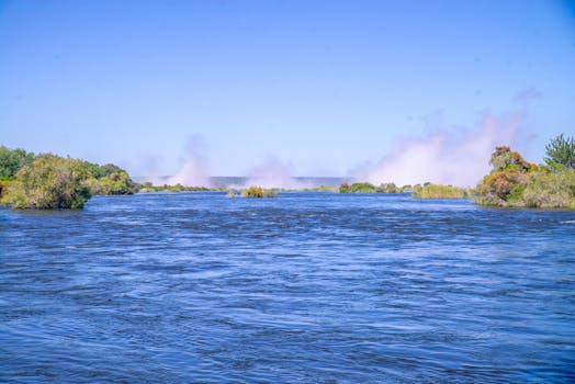 Beautiful river scene with mist, vibrant greenery, and clear blue sky.