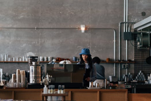 A barista wearing a blue hat operates a coffee machine in a stylish Yokosuka café setting.