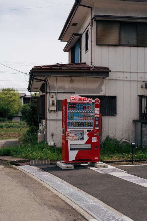 Free A red vending machine stands outside a traditional Japanese house, capturing everyday Japan. Stock Photo