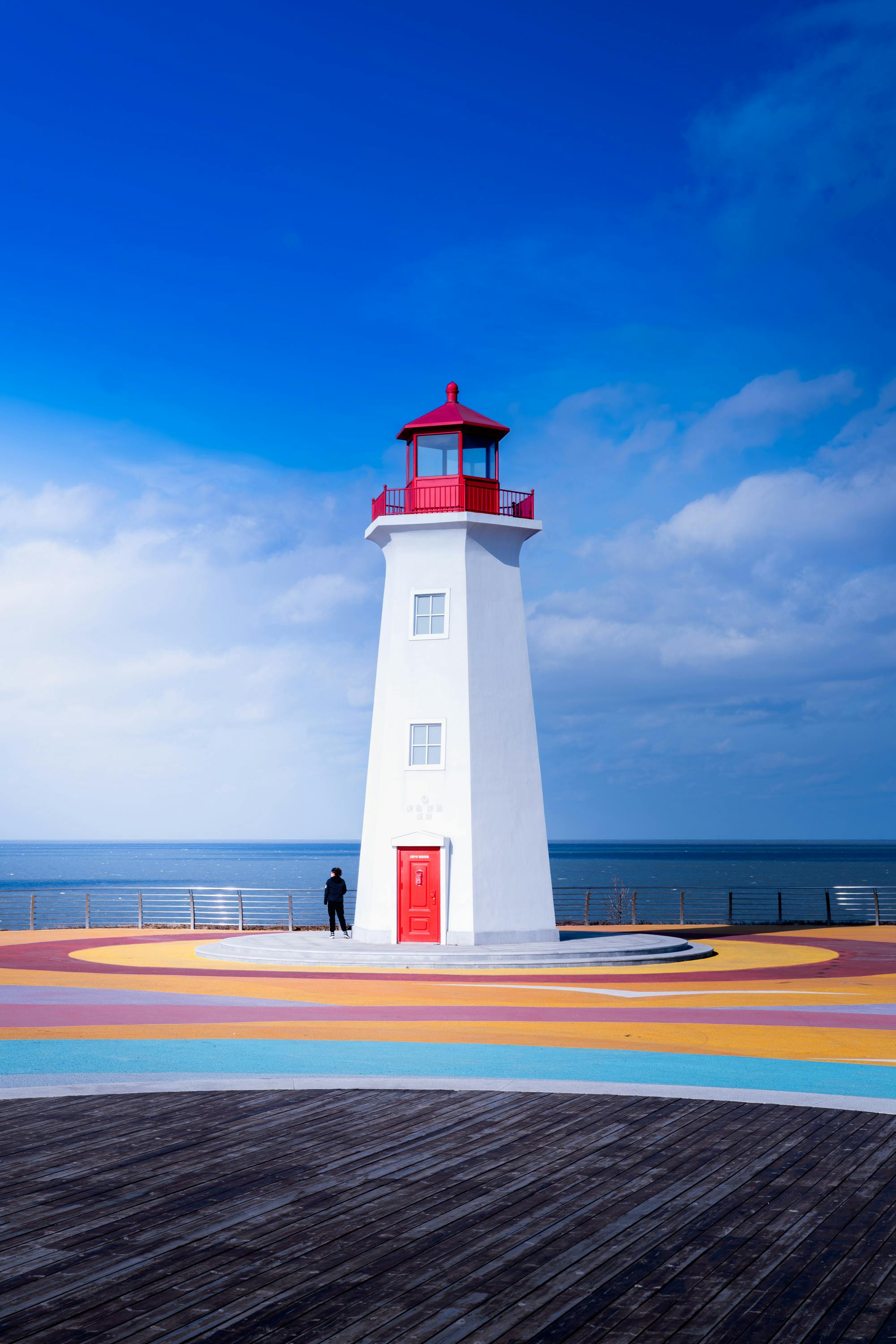 Dramatic lighthouse under blue sky on a colorful platform by the sea, perfect for coastal themes.