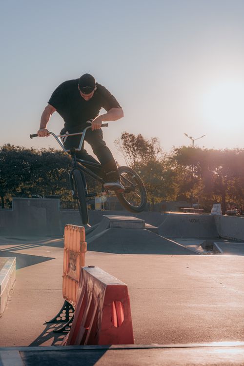 Free A BMX rider performs an impressive trick at a skatepark during sunset, capturing the energy of freestyle biking. Stock Photo