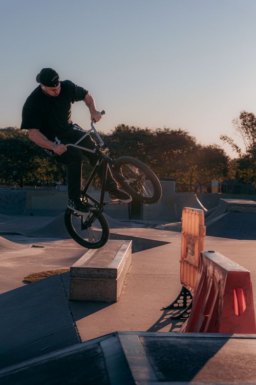 Free BMX rider performing a trick on a ramp at a skatepark during sunset. Stock Photo