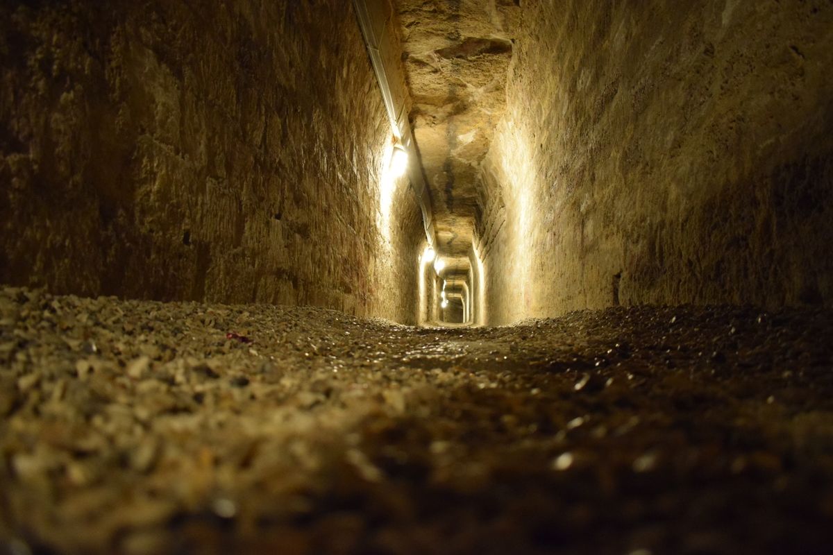 A dim stone corridor deep inside an Egyptian catacomb, lit by small lamps