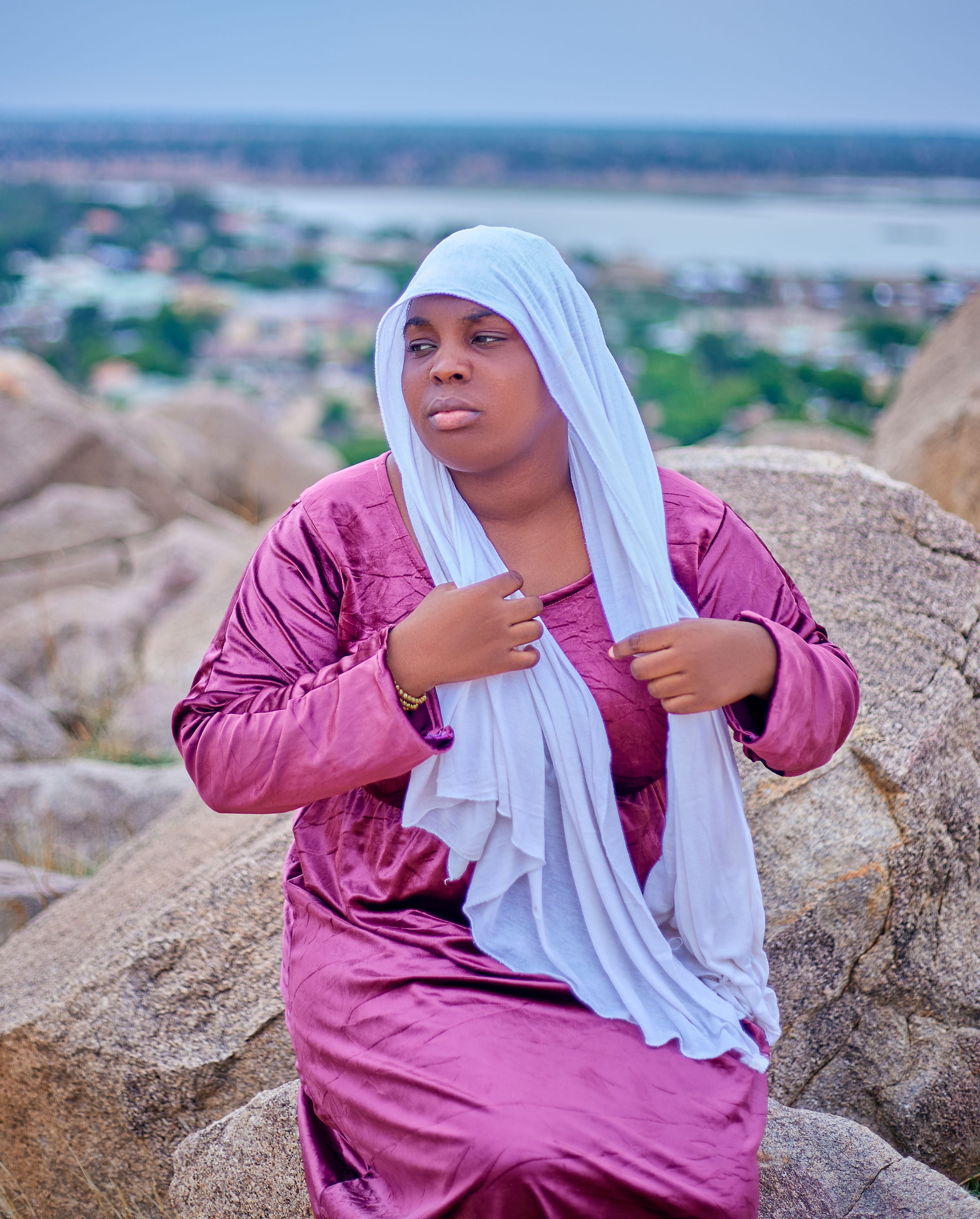 Woman in hijab sitting on rocks with scenic view, serene and contemplative.