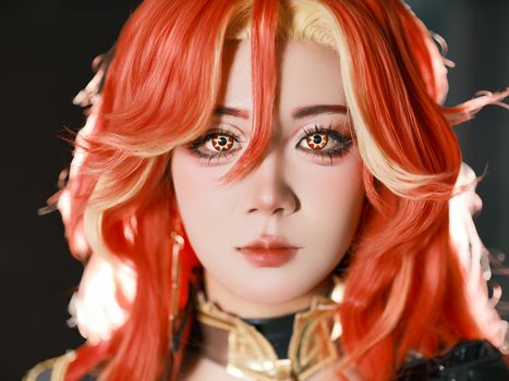 Close-up of a person in cosplay with striking orange and blonde hair, detailed eye makeup.