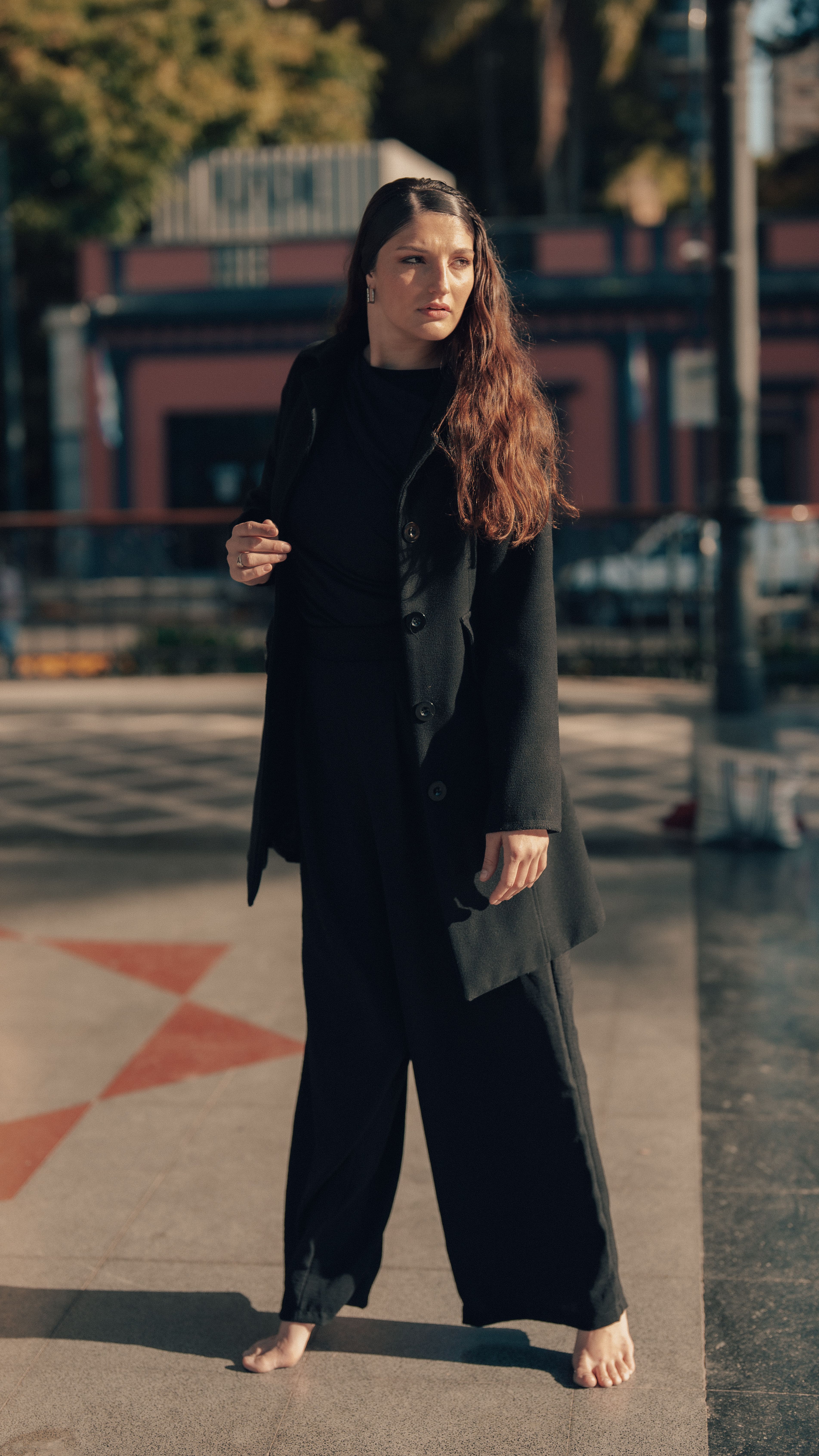 grátis Mulher vestida de preto está de pé, confiante e descalça, em uma praça de Buenos Aires, exalando elegância. Foto profissional