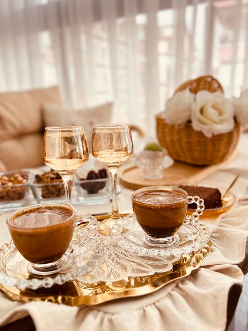 Free A cozy setup with coffee, desserts, and wine glasses, adorned with flowers, creating a warm and inviting ambiance. Stock Photo