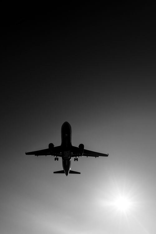Free Silhouette of an airplane soaring above Buenos Aires with the sun in the background, captured in monochrome. Stock Photo