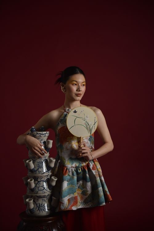 Free Portrait of a woman in traditional Asian attire holding a bamboo fan beside ceramic vases. Stock Photo