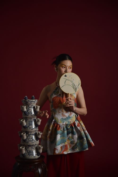 Free Woman in traditional Asian attire holding a decorative fan beside a porcelain vase set. Stock Photo
