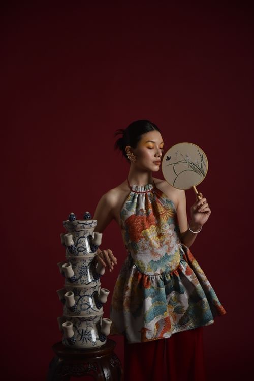 Free A fashionable woman poses with a fan and traditional ceramic set against a dark backdrop. Stock Photo