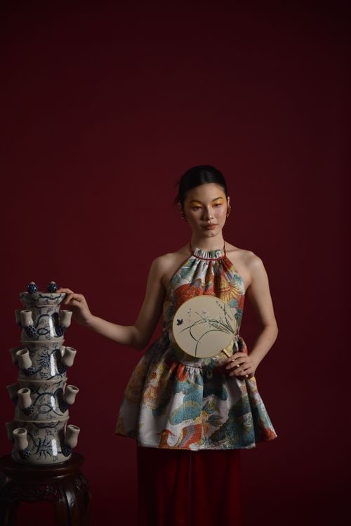 Free Portrait of a woman in traditional attire holding a Chinese fan with ceramic teapots. Stock Photo