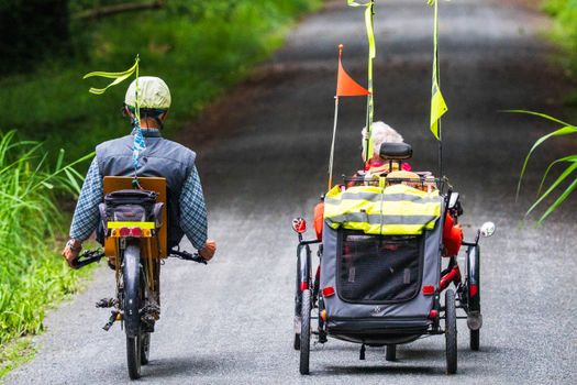 Two adults ride recumbent trikes with safety flags on a scenic countryside road, promoting outdoor exercise.