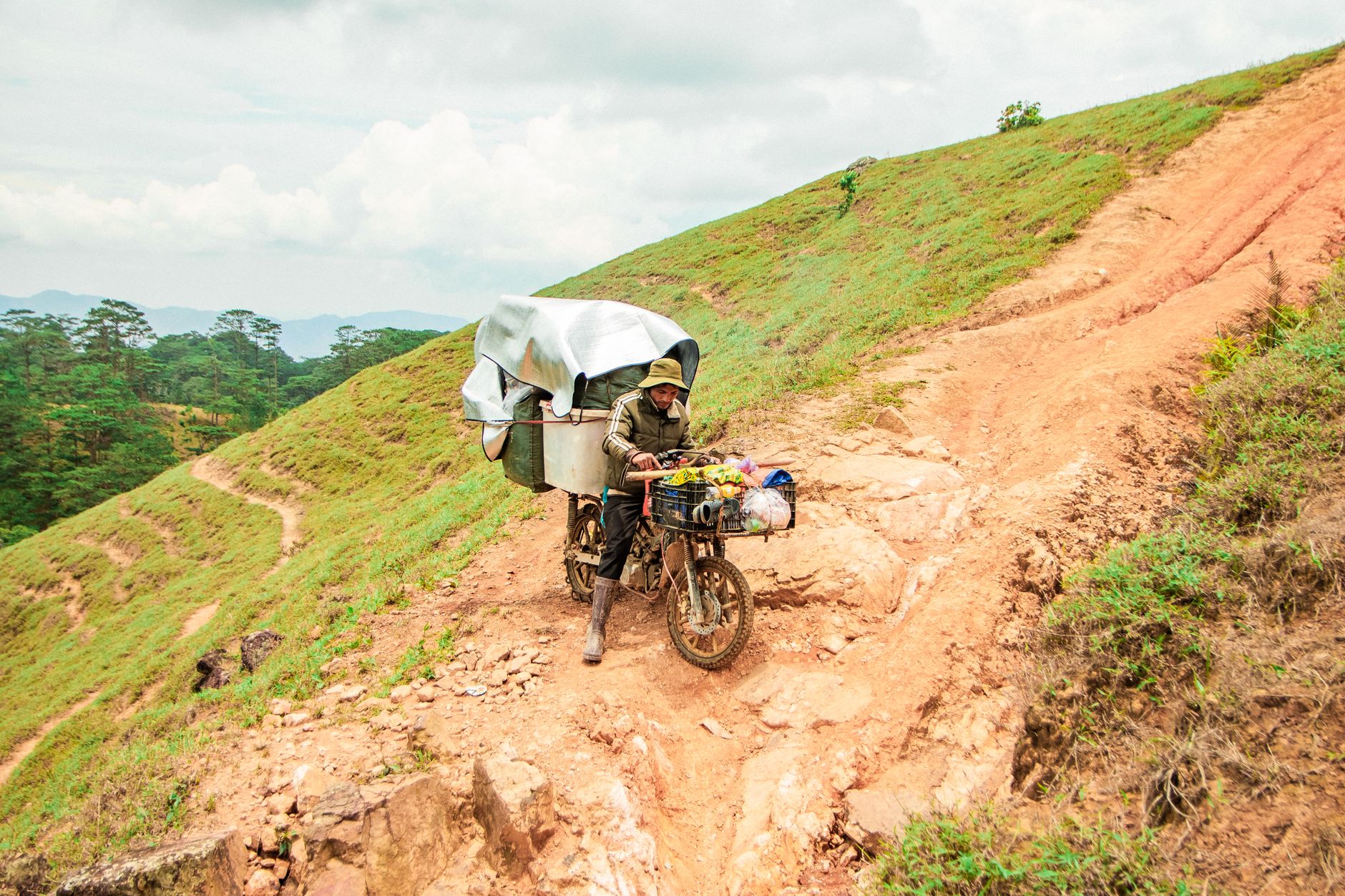 Motorcyclist navigating a steep hill in Lâm Đồng, Vietnam, with goods loaded. Rural and adventurous vibe.