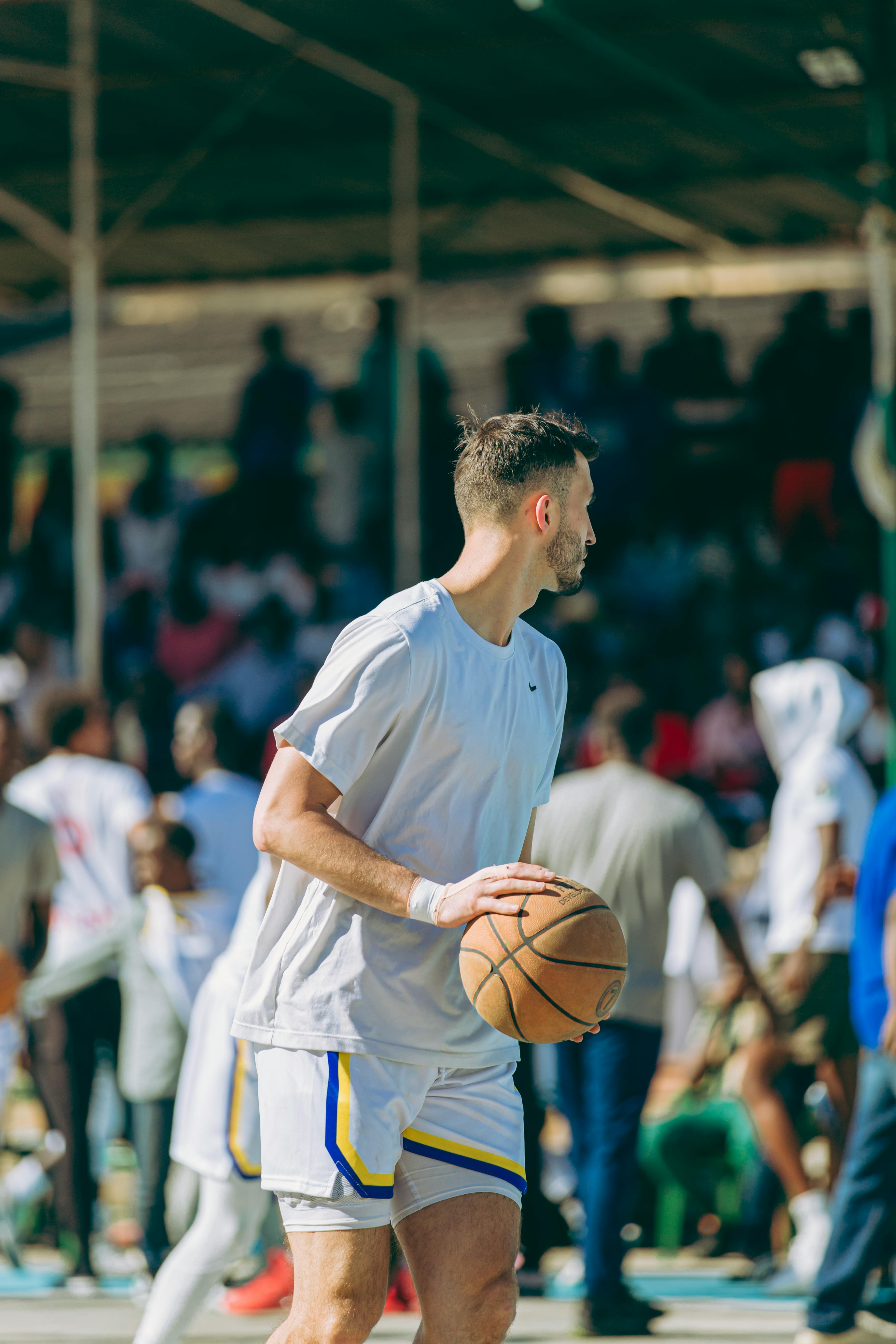 Young adult playing basketball on an outdoor court with a crowd in the background.