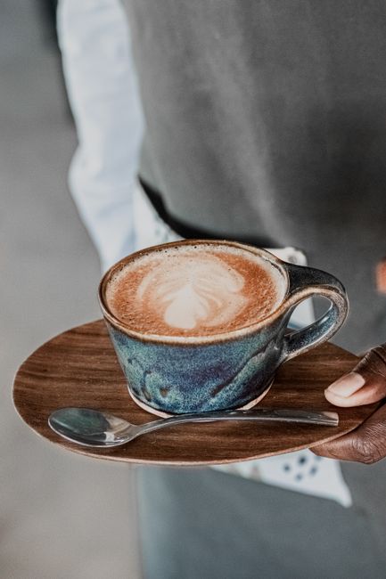 A barista presents a cappuccino with heart-shaped latte art in a blue ceramic cup.