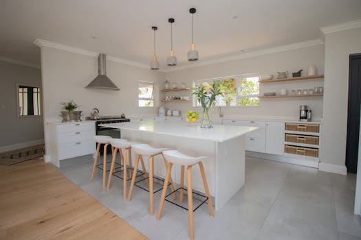 Bright and modern minimalist kitchen featuring a large island, bar stools, and sleek appliances.