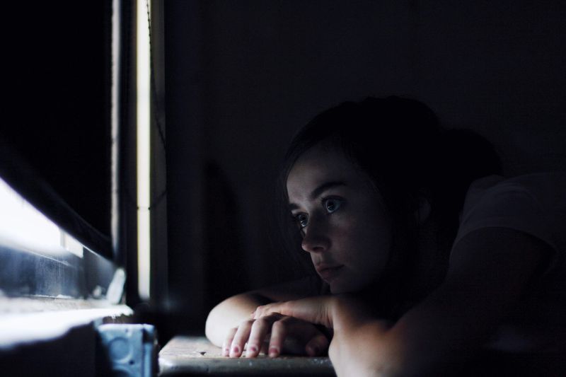 A woman sitting alone by a window in dim light