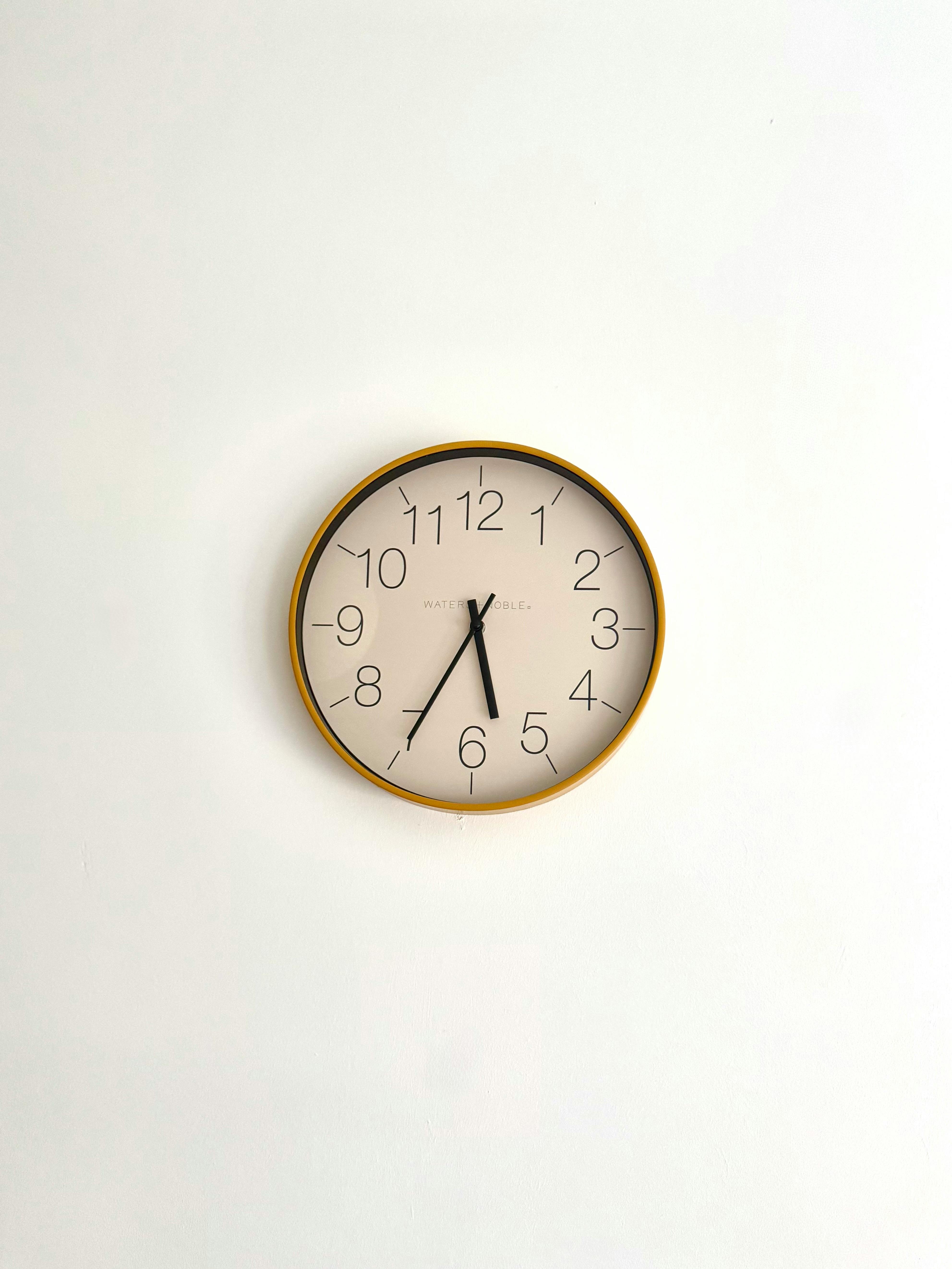 Simple round clock with black numerals on a white wall, showing 5:40.