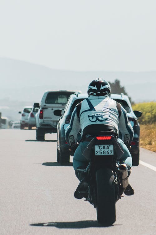 Back view of anonymous male biker driving motorcycle on asphalt road among cars