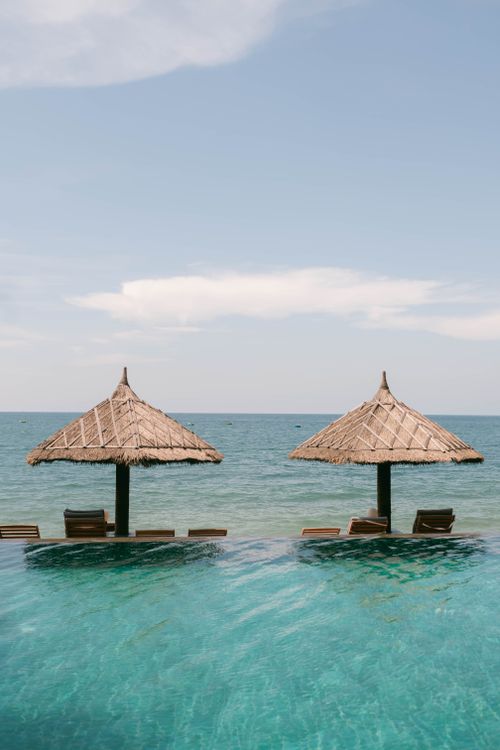Free Peaceful beach scene featuring two thatched umbrellas by the sea, perfect for relaxation. Stock Photo