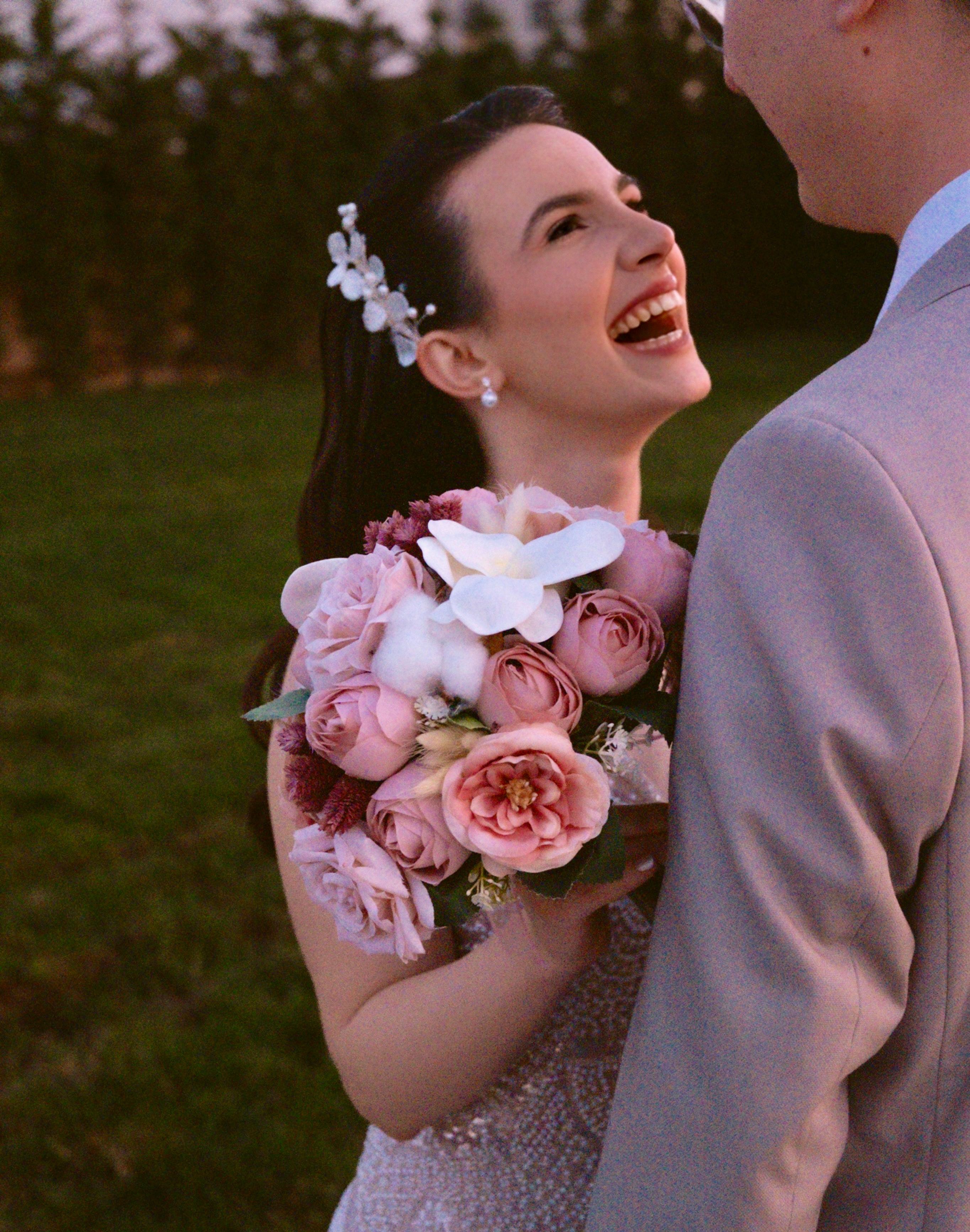 Joyful bride with floral bouquet shares a moment with the groom outdoors at sunset.
