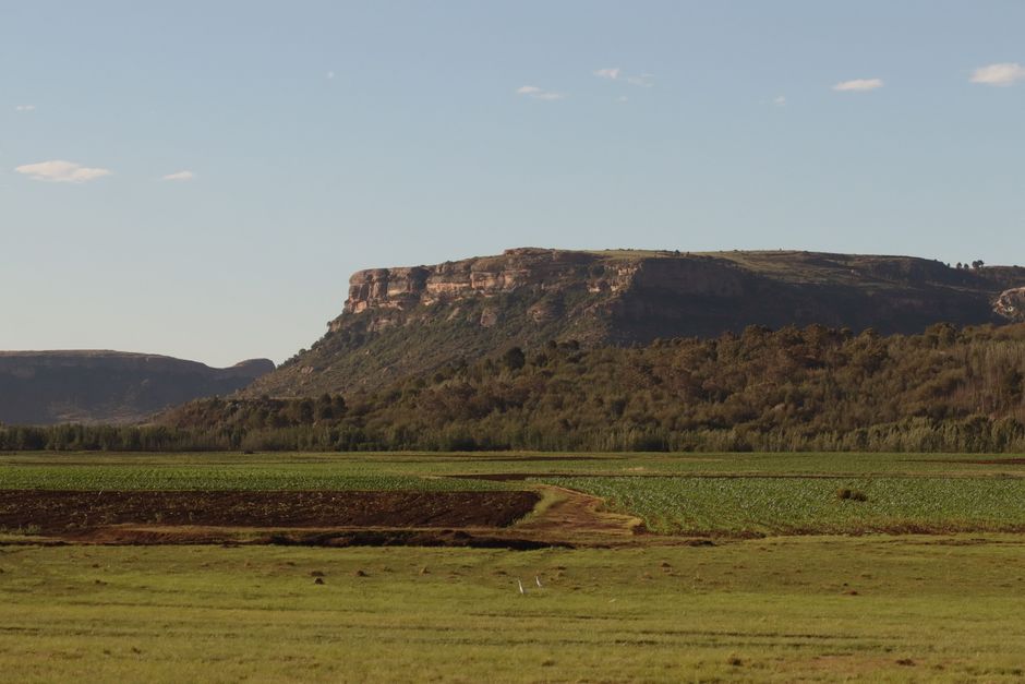Serene view of Lesotho's lush fields and rugged mountains under clear blue skies.