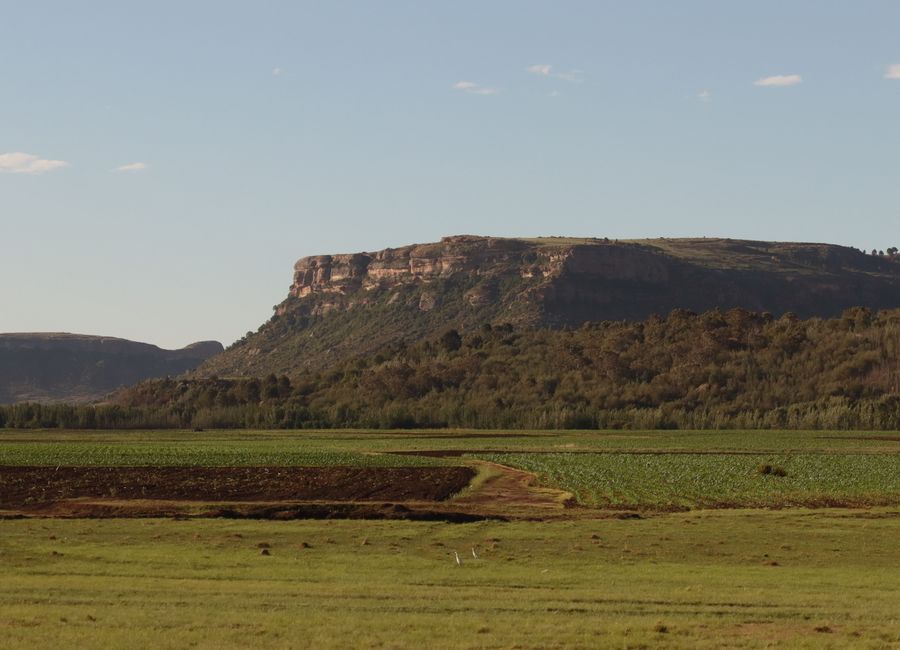 Serene view of Lesotho's lush fields and rugged mountains under clear blue skies.