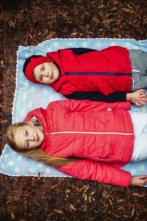 Siblings in Red Jacket Lying on Blanket