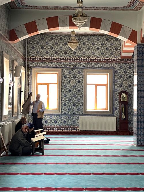 Free Ornate mosque interior with worshippers, featuring detailed tilework and a clock. Stock Photo