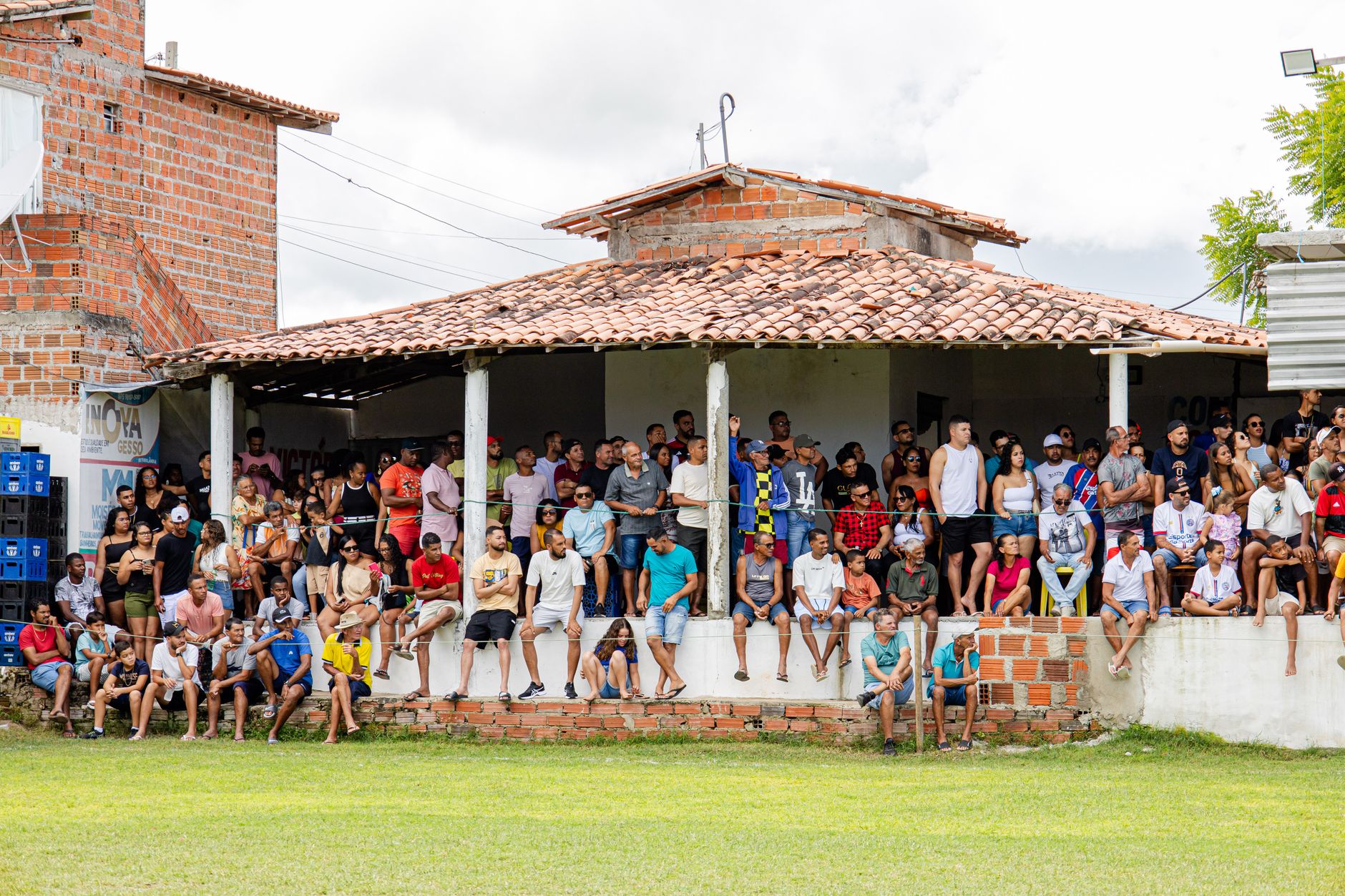 A large and diverse group of people gathered at an outdoor venue with rustic brick architecture, observing an event.