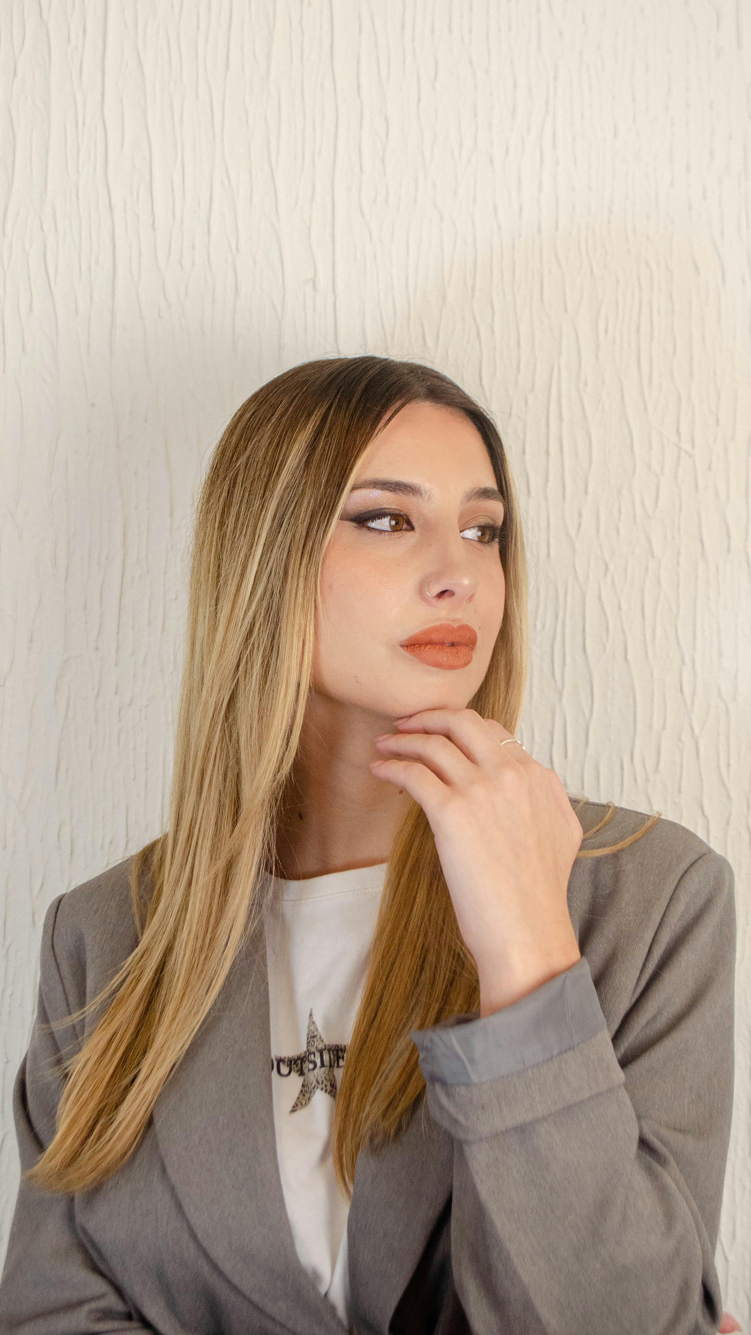 Young woman with stylish outfit and makeup posing indoors with neutral background.