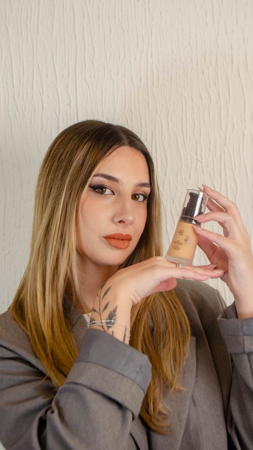Free Woman in a stylish grey outfit showcasing a foundation bottle. Stock Photo