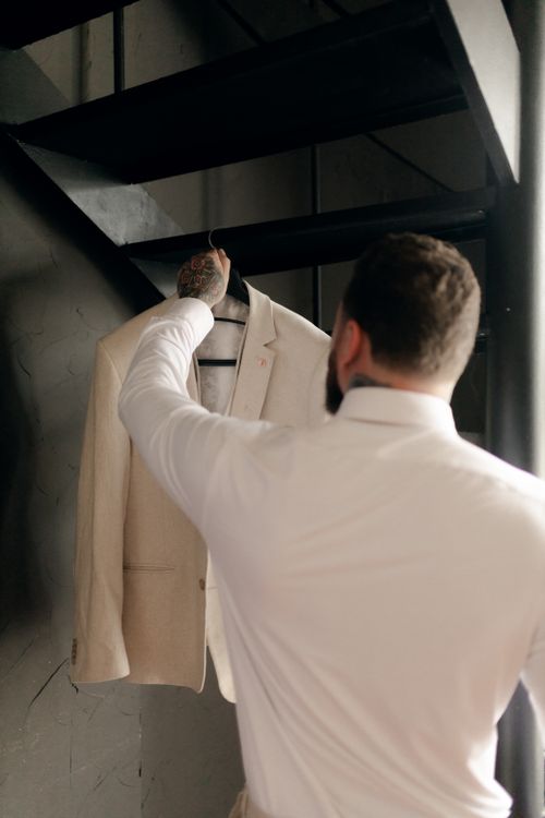 Free Bearded man choosing a suit jacket from stairway hanger, showcasing elegance. Stock Photo