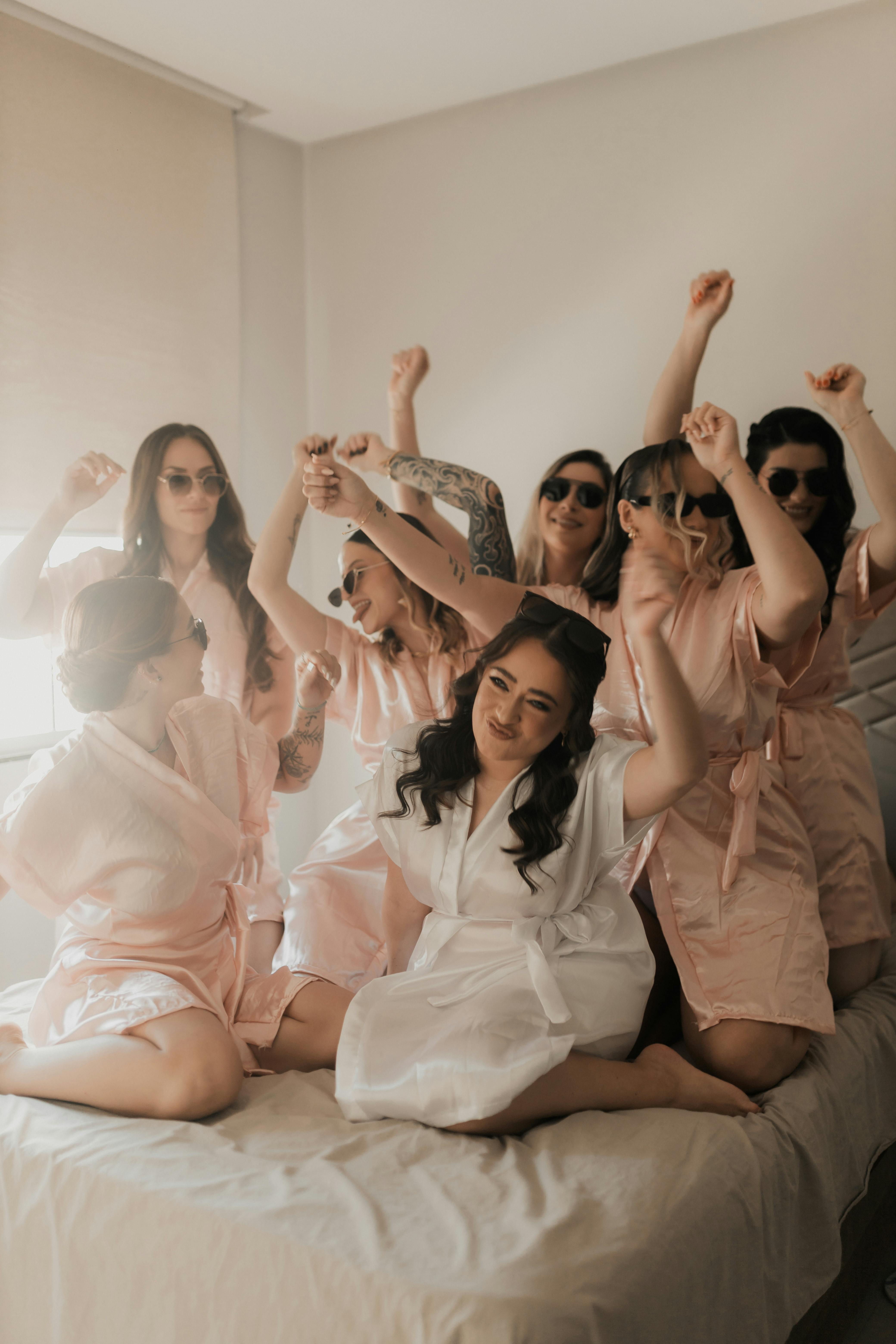 A joyful bridal party in satin robes celebrating on a bed indoors, creating a warm and fun atmosphere.