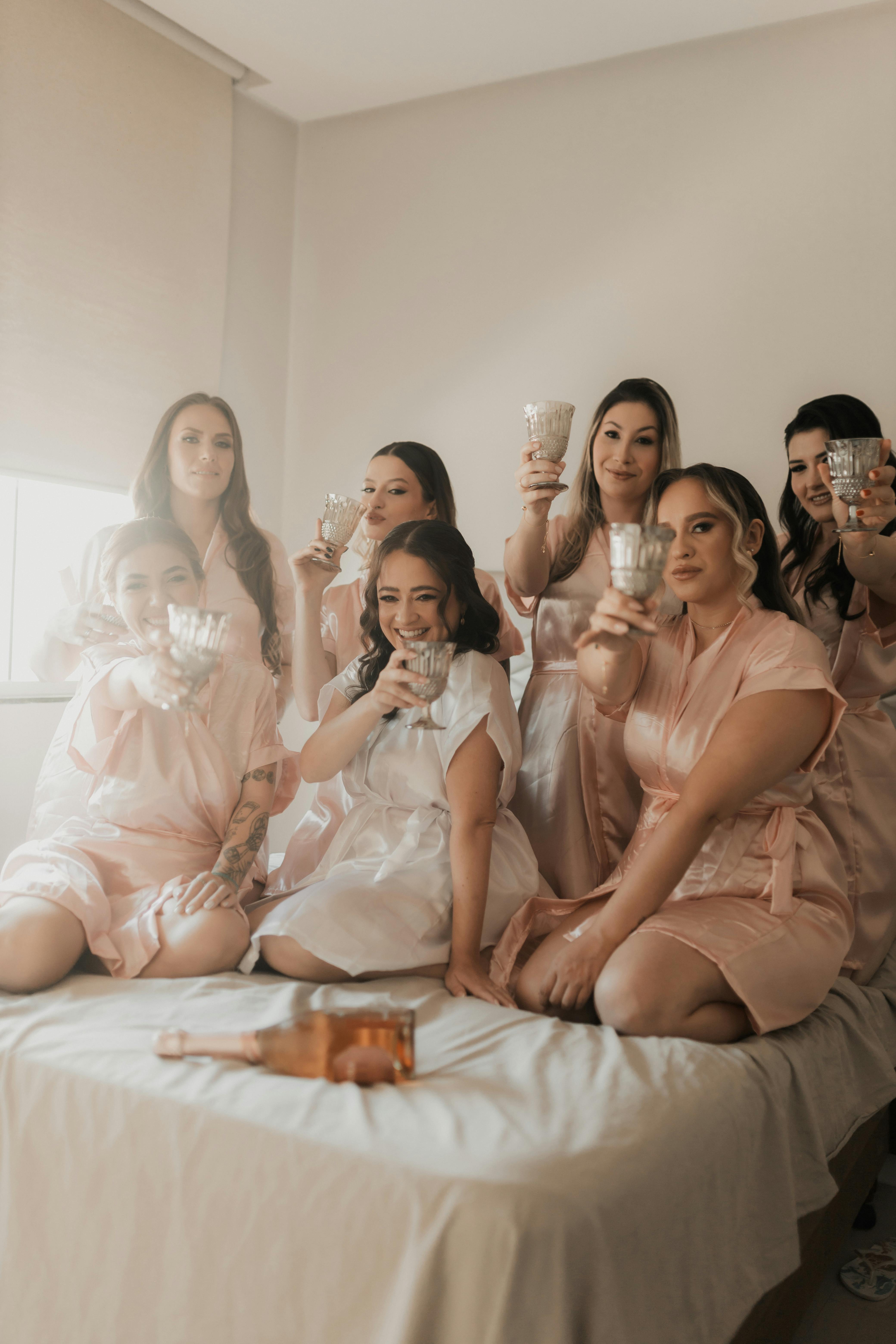 A group of bridesmaids in robes celebrating with champagne, captured indoors.