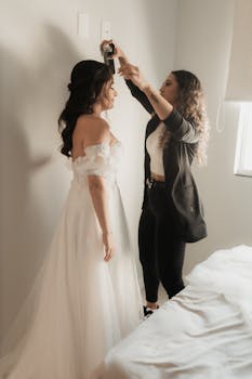 A hairstylist prepares a bride for her wedding in a serene indoor setting.