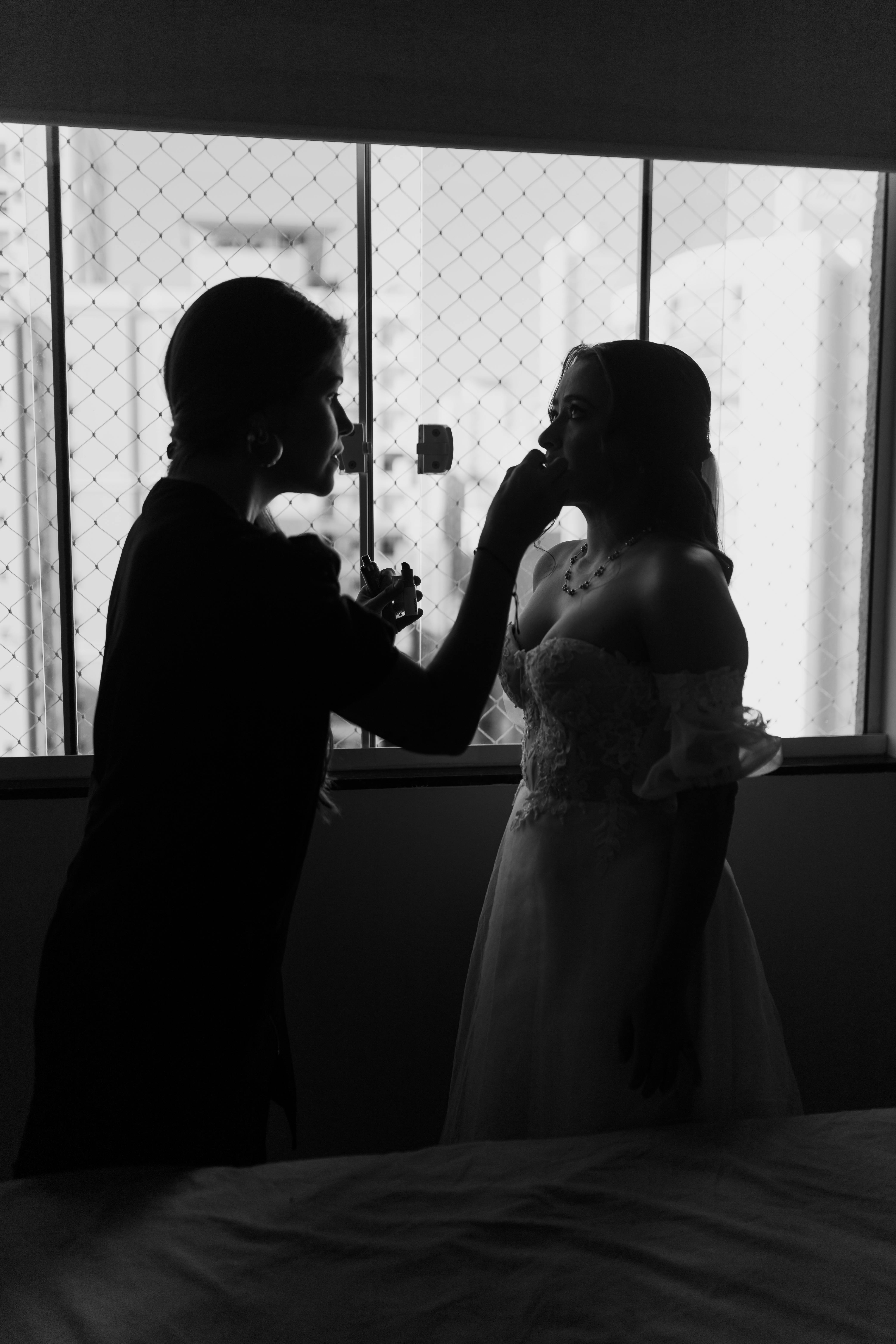 Black and white silhouette of a bride being assisted by a makeup artist in preparation for her wedding day.