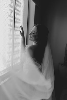 A serene black and white portrait of a bride by a window, exuding grace and tranquility.