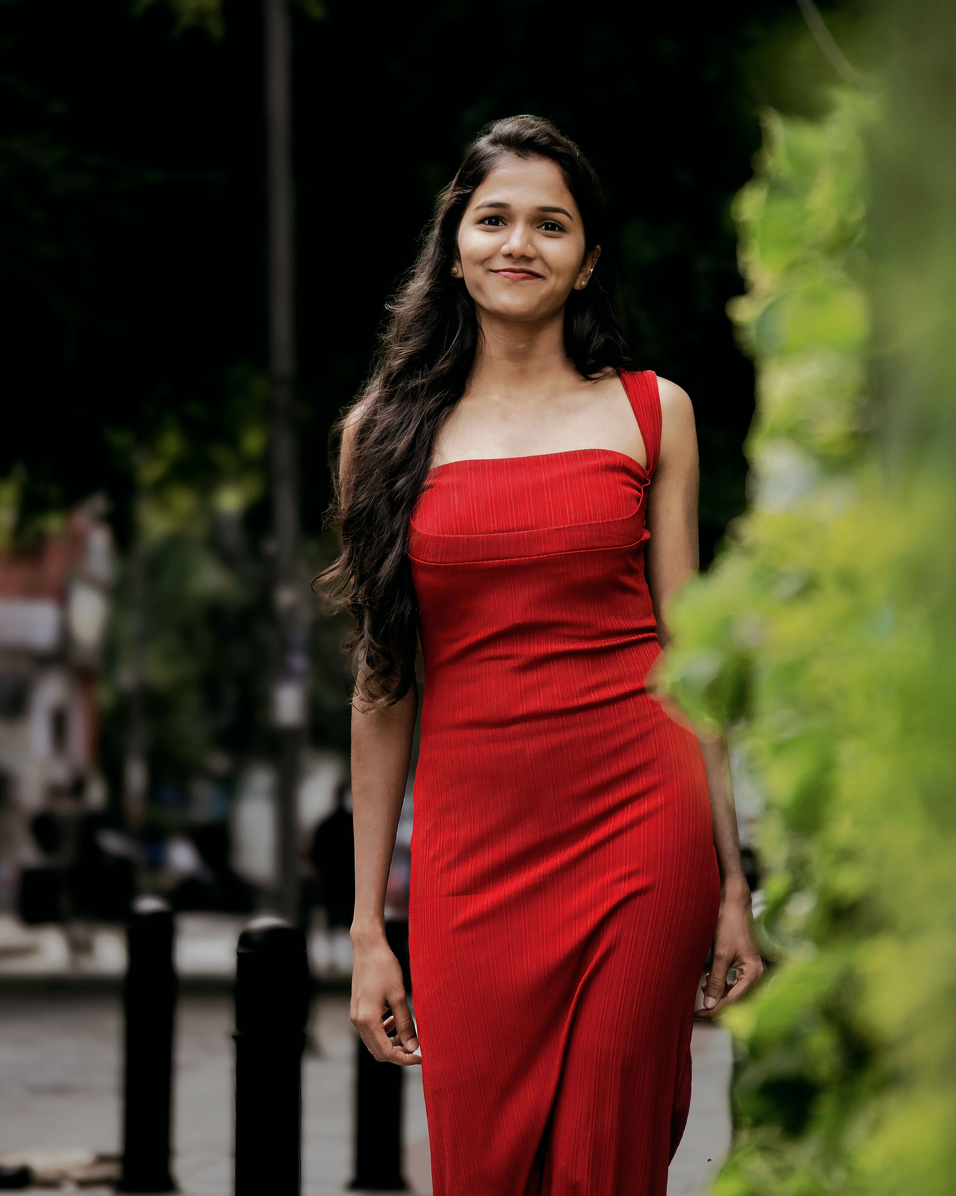Confident woman in red dress smiles while strolling outside on a summer day.